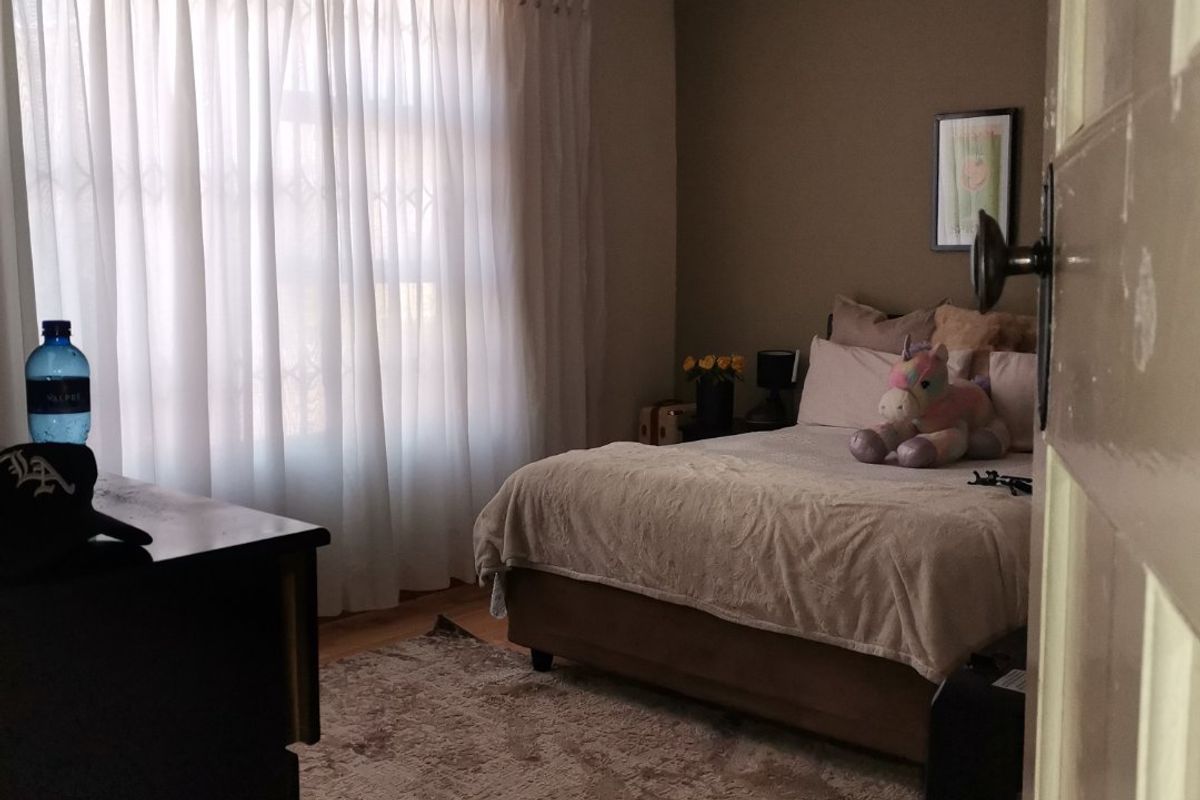 A cozy bedroom featuring laminate flooring, neutral wall tones, and large windows with curtain tracks, offering a comfortable and functional living space.