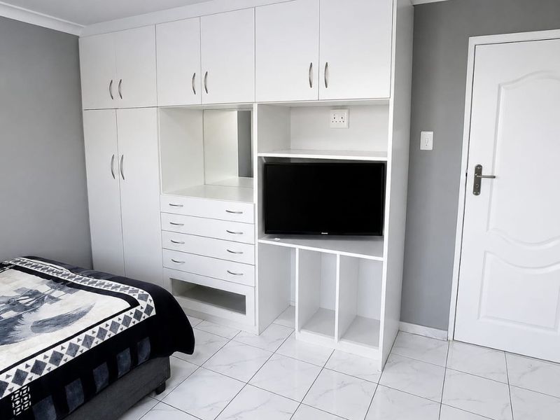 A well-maintained bedroom featuring white built-in cabinetry with integrated storage and shelving, complemented by modern white marble-effect floor tiles.