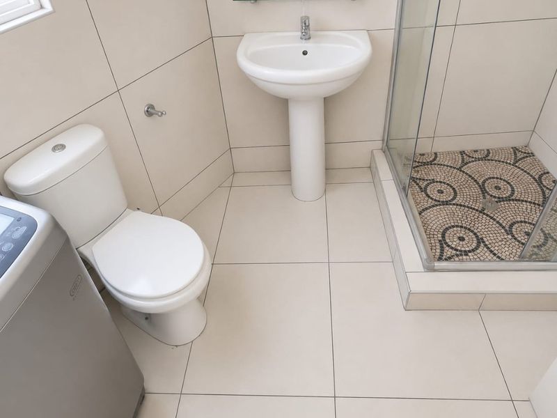 A clean, modern bathroom featuring a pedestal basin, toilet, and a glass-enclosed shower with decorative mosaic floor tiling.
