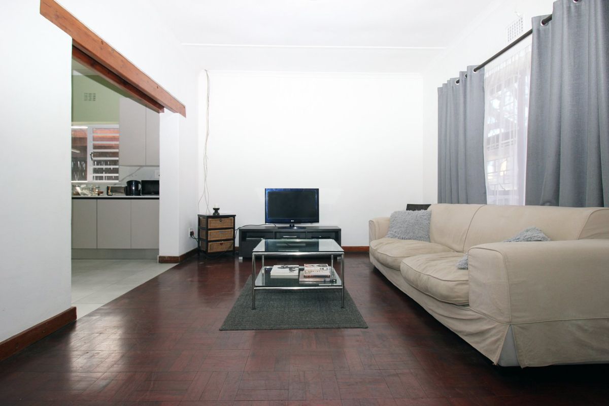 A living room featuring dark parquet flooring and a wide opening leading into the kitchen area.