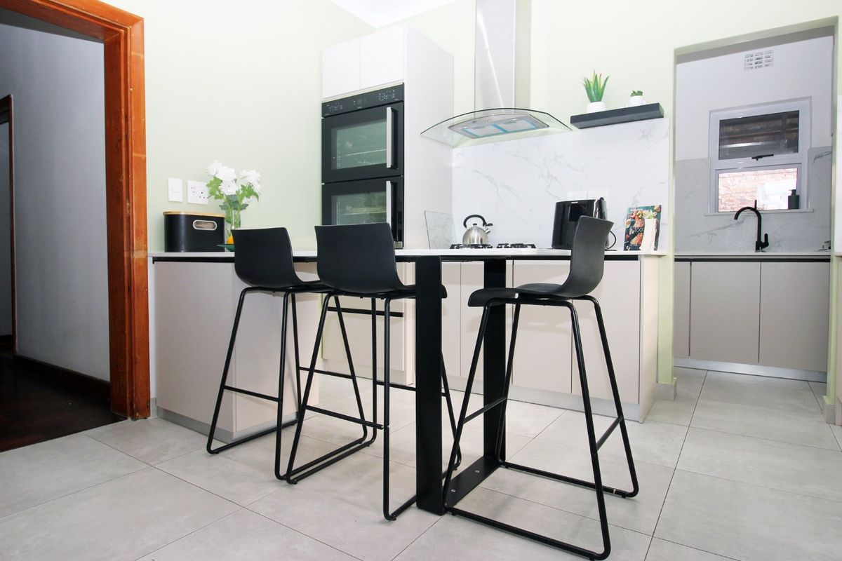 Modern kitchen featuring a built-in double oven, sleek cabinetry, marble-look splashback, and a functional breakfast bar area with tiled flooring.