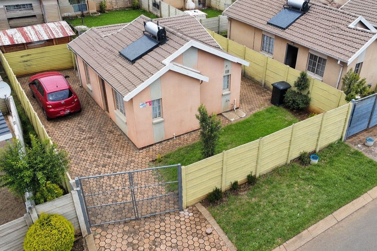 Aerial view of a detached residential property featuring a paved driveway, solar water heating system, and enclosed garden area with precast boundary walls.