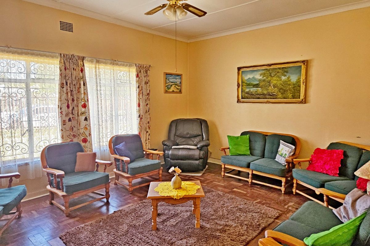 A traditional living room featuring classic parquet flooring, a ceiling fan, and large windows fitted with security bars.