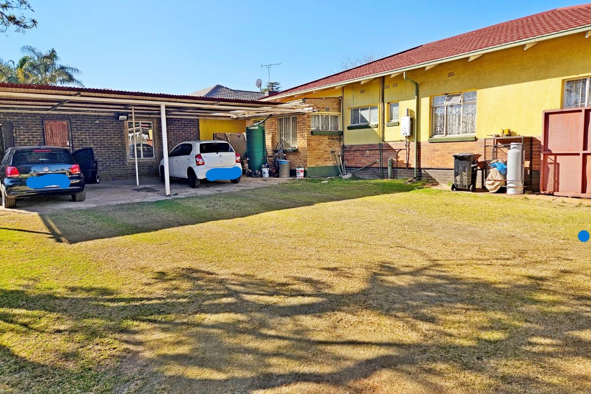 Rear exterior view of the property featuring a large lawn, a covered carport area, and brick and plaster wall finishes.