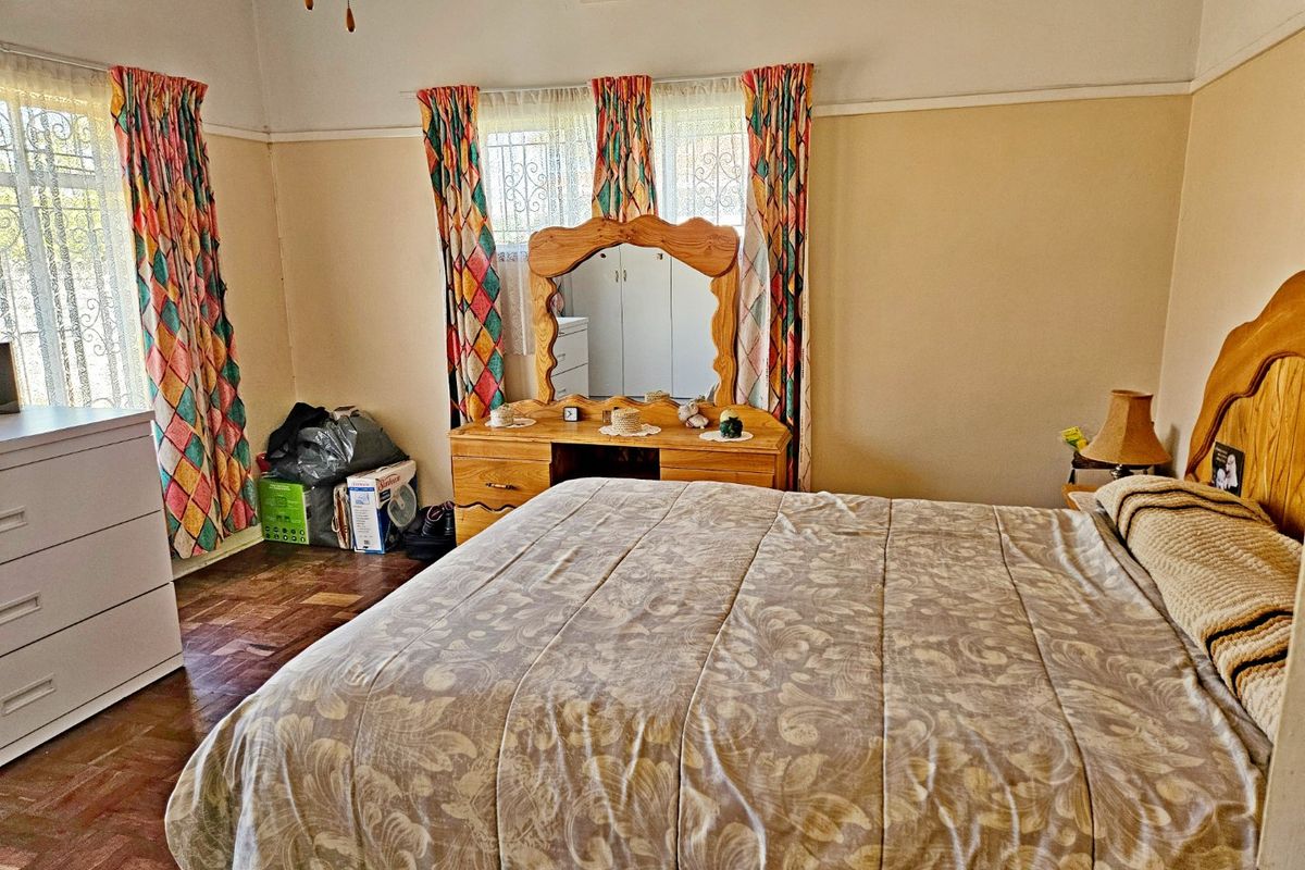 A bedroom featuring parquet flooring, security bars on the windows, and a ceiling vent. The space is dated and would benefit from cosmetic updates.