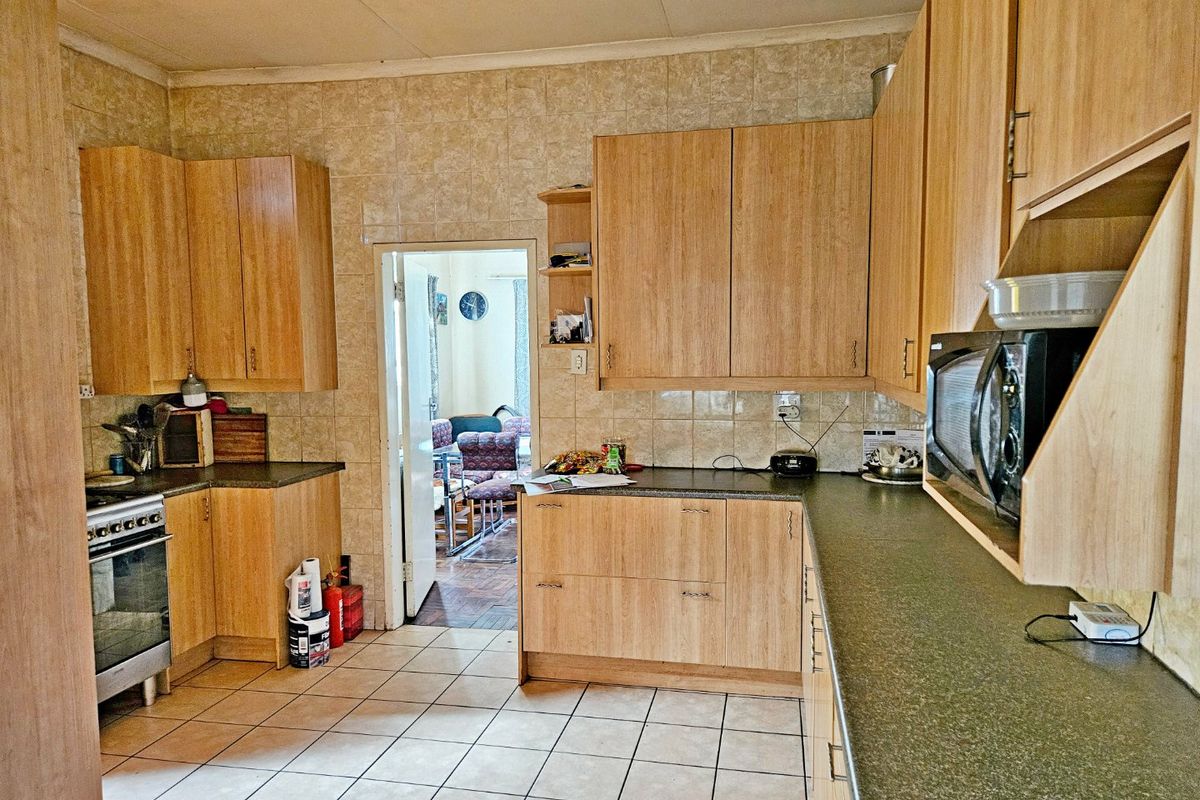A functional kitchen featuring laminate cabinetry, stone-look countertops, tiled splashbacks, and a freestanding oven, offering a practical layout with potential for modernization.