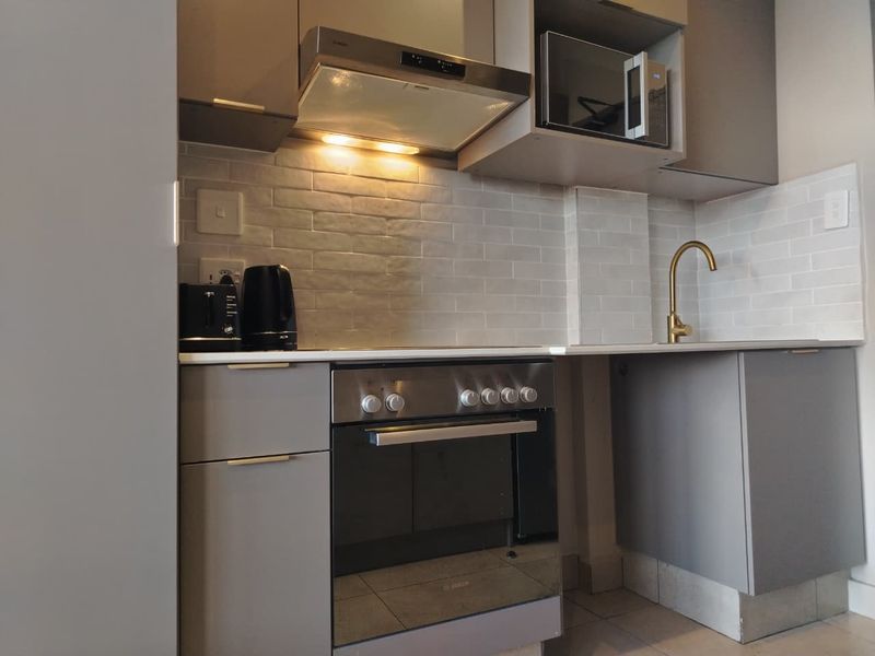 Modern kitchen featuring grey cabinetry, subway tile backsplash, brass faucet, and integrated appliances including an oven, extractor fan, and microwave.