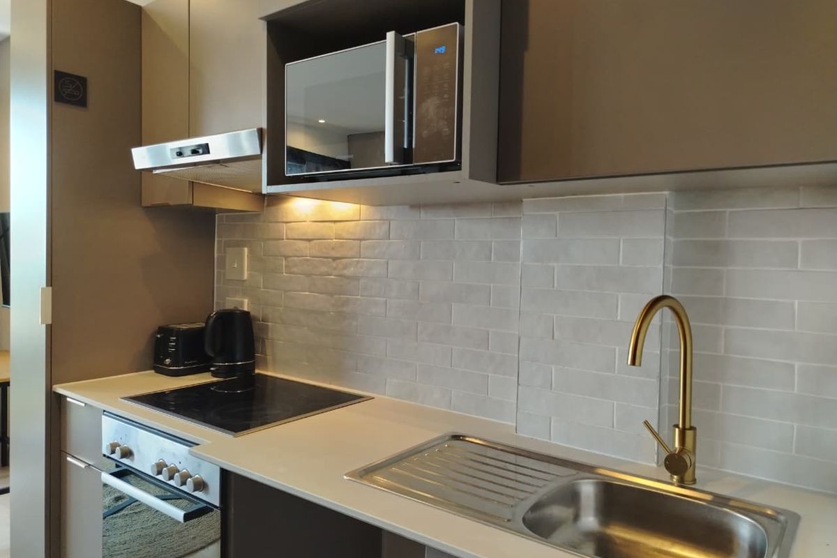 Modern kitchen featuring sleek cabinetry, subway tile backsplash, stone countertops, integrated appliances, and a stylish gold-tone faucet.