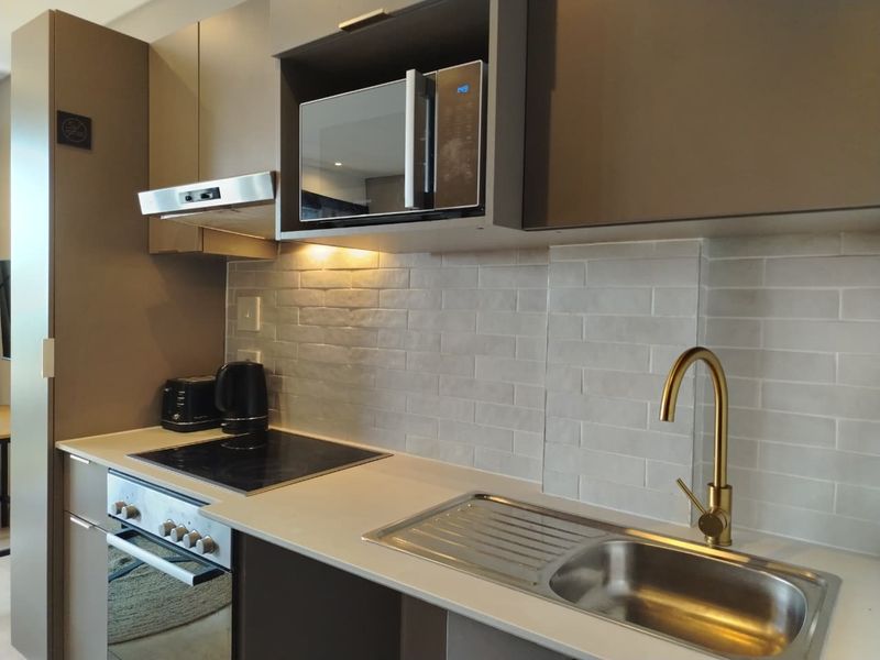 Modern kitchen featuring sleek cabinetry, subway tile backsplash, stone countertops, integrated appliances, and a stylish gold-tone faucet.