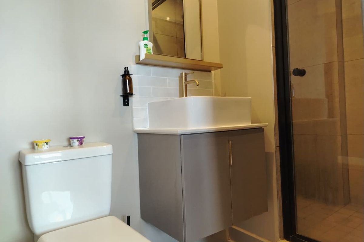 Modern bathroom featuring a floating vanity with a vessel sink, brass fixtures, subway tile backsplash, and a glass-enclosed shower.
