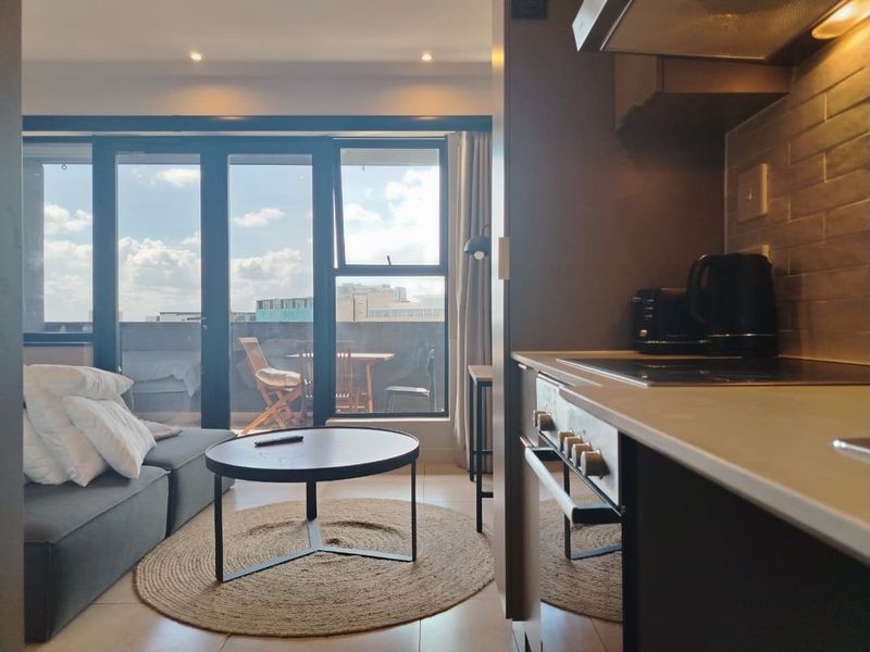 Modern open-plan living area featuring a compact kitchen with built-in appliances, tiled flooring, and large sliding doors leading to a private balcony.