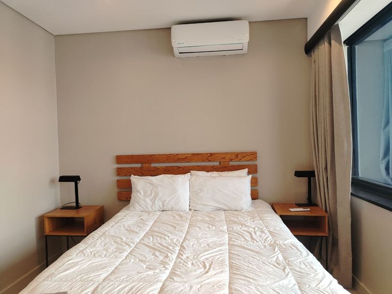 A well-maintained bedroom featuring a wall-mounted split-system air conditioner and a large window with floor-to-ceiling curtains.