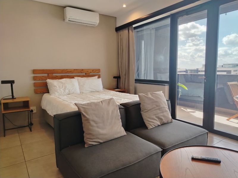 Modern bedroom featuring tiled floors, a wall-mounted air conditioning unit, and large sliding glass doors providing direct access to a private balcony.