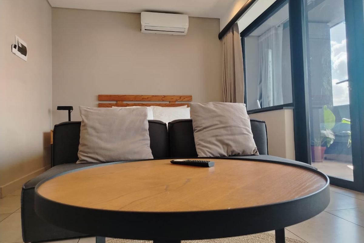 A modern bedroom featuring a split-system air conditioner, recessed lighting, and large sliding glass doors providing access to an outdoor balcony area.