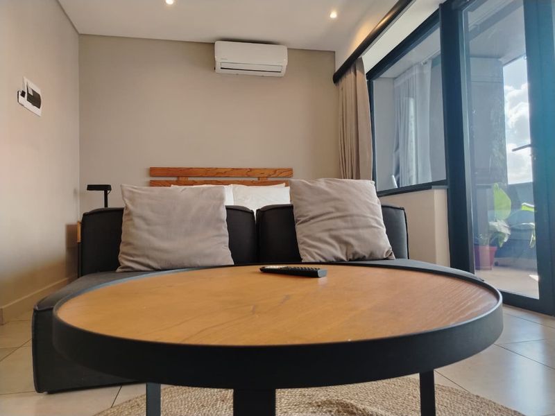 A modern bedroom featuring a split-system air conditioner, recessed lighting, and large sliding glass doors providing access to an outdoor balcony area.