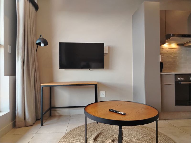 Modern open-plan living area featuring a compact kitchen with built-in oven, extractor fan, and neutral tiled flooring throughout.