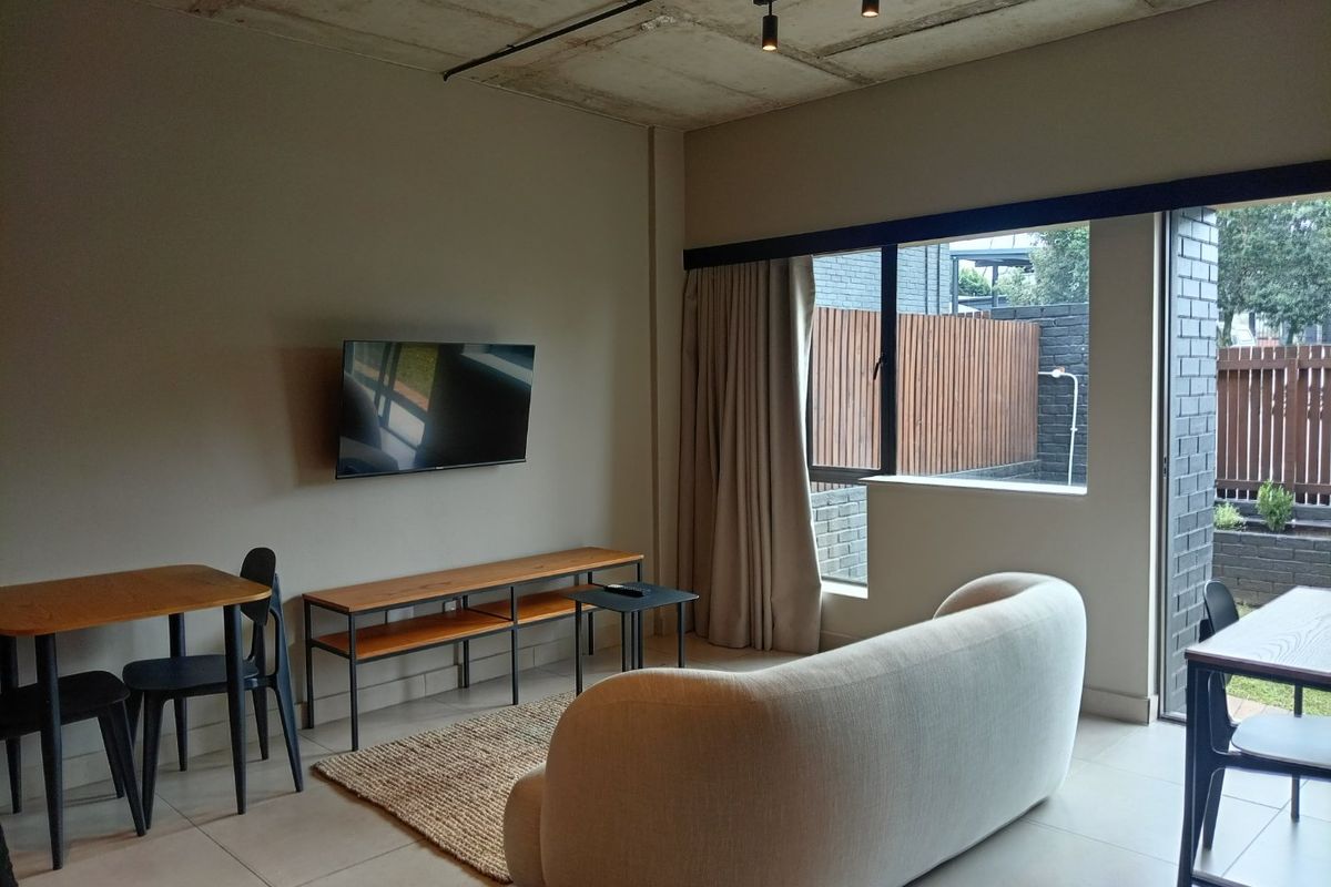 Modern living area featuring an exposed concrete ceiling, track lighting, and large sliding glass doors providing access to an outdoor space.