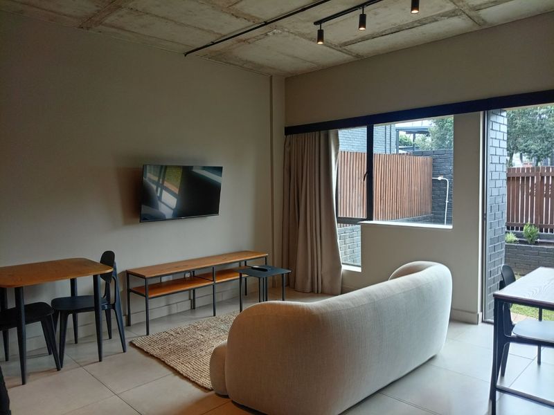 Modern living area featuring an exposed concrete ceiling, track lighting, and large sliding glass doors providing access to an outdoor space.
