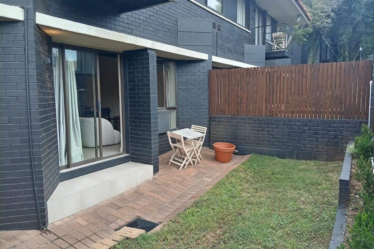 A private rear courtyard featuring a paved patio area, dark brick exterior walls, and a timber privacy fence.
