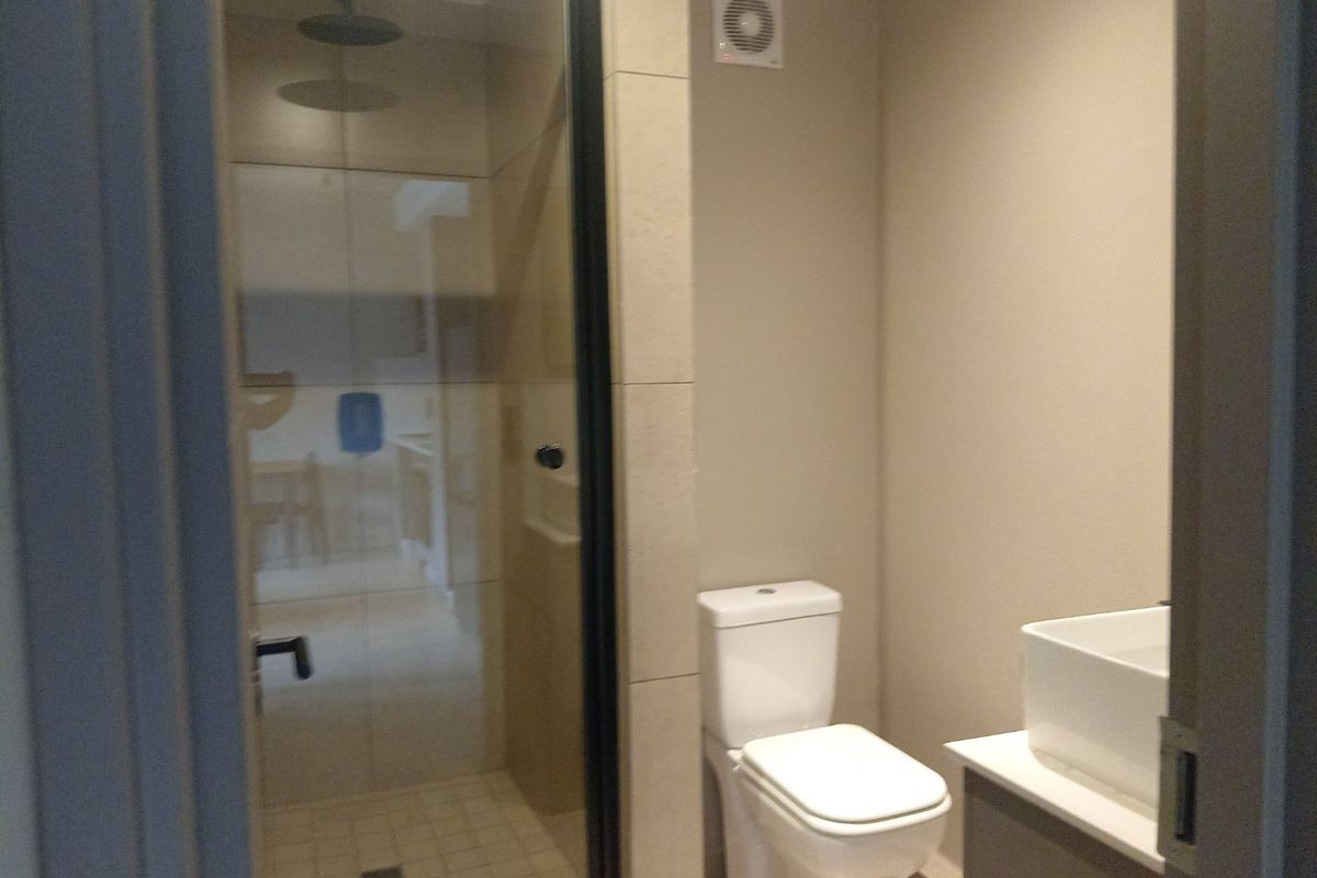 A modern bathroom featuring a glass-enclosed shower with a rain shower head, a white toilet, and a contemporary vanity basin.