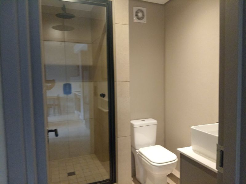 A modern bathroom featuring a glass-enclosed shower with a rain shower head, a white toilet, and a contemporary vanity basin.