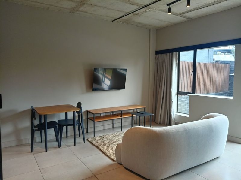 A modern living room featuring an exposed concrete ceiling, track lighting, and large windows that provide ample natural light.
