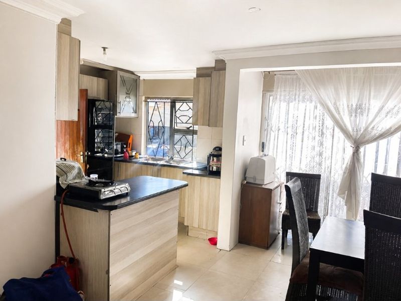 Open plan kitchen and dining area featuring light wood-finish cabinetry, laminate countertops, and tiled flooring with access to an outdoor space.