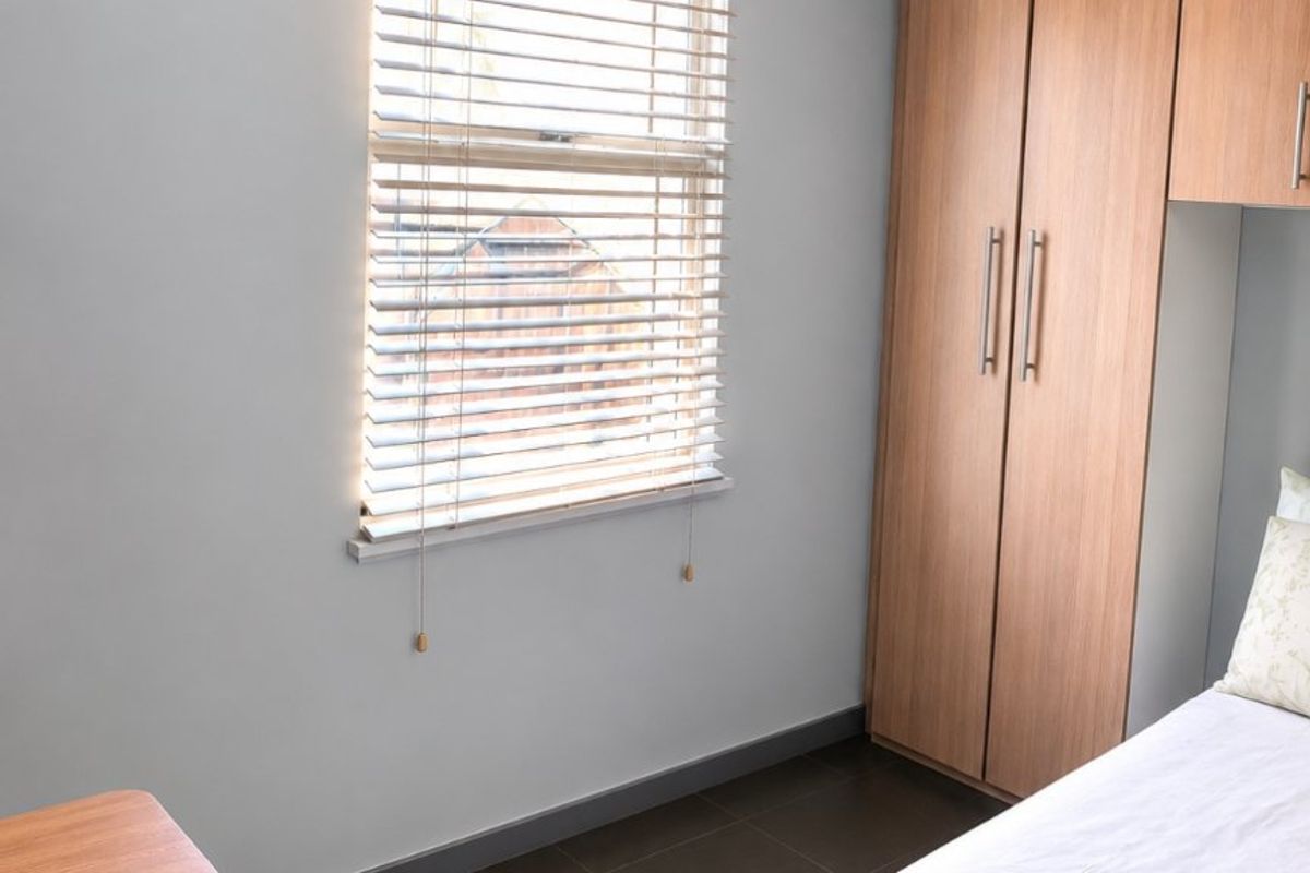 A well-maintained bedroom featuring built-in wooden wardrobes, tiled flooring, and venetian blinds on the window.