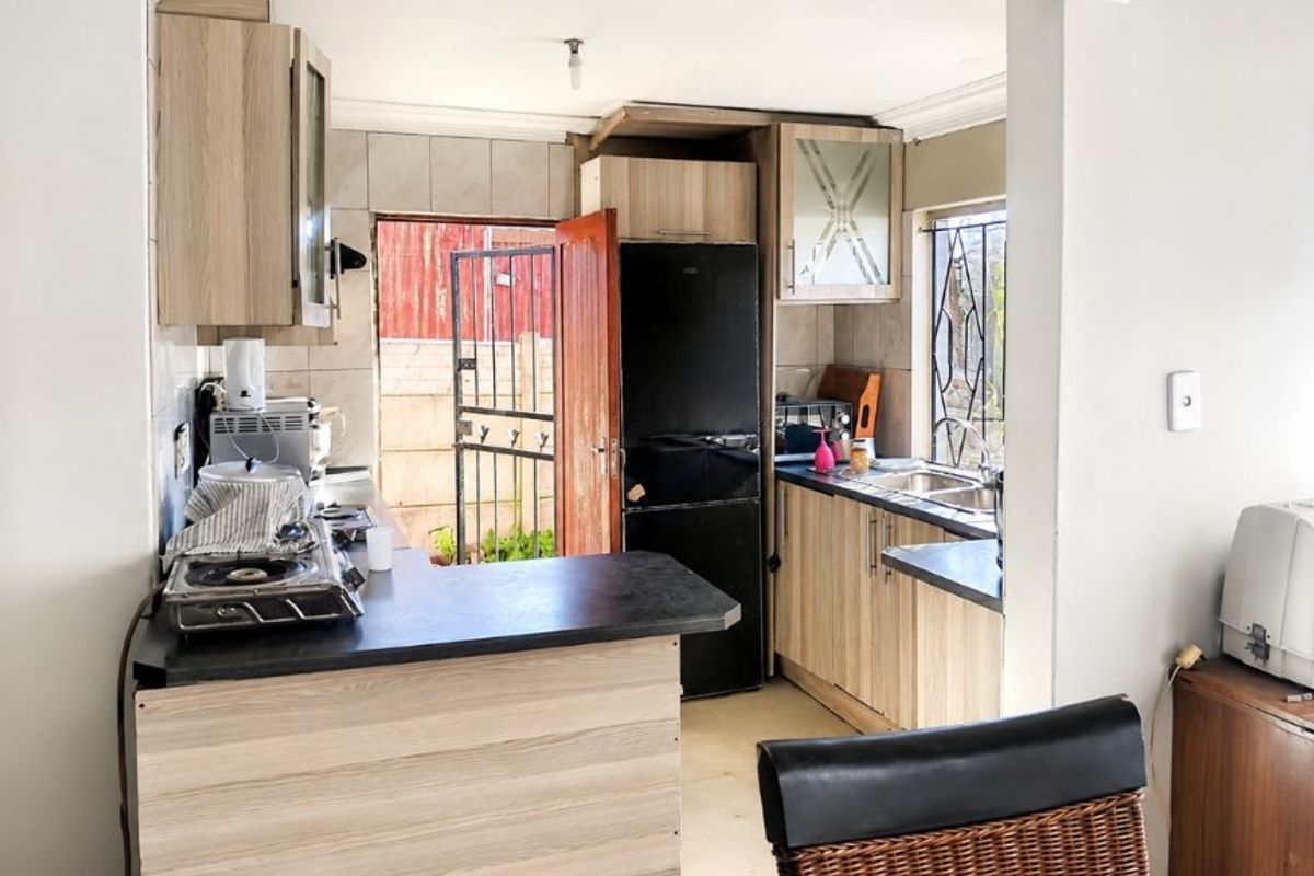 Compact kitchen featuring light wood-look cabinetry, dark laminate countertops, tiled backsplash, and direct access to the exterior via a security gate.