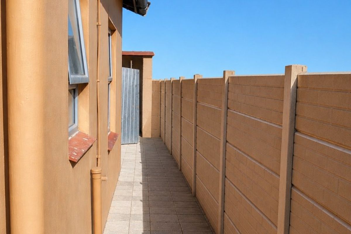 A narrow side walkway featuring tiled flooring, a precast concrete boundary wall, and an external water tap along the side of the house.