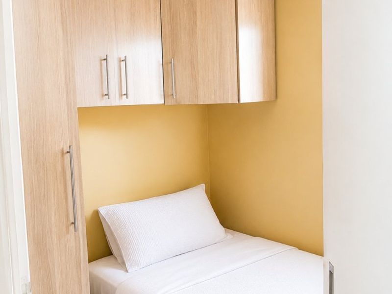 A compact bedroom featuring light wood-toned built-in cabinetry and overhead storage cupboards.