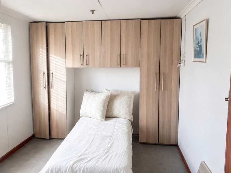 A bedroom featuring built-in wooden cupboards with overhead storage units and tiled flooring.