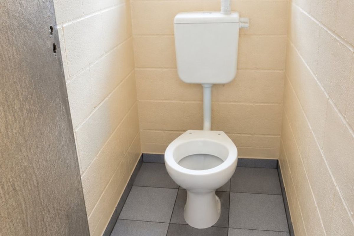 A small, functional bathroom featuring a standard toilet, tiled flooring, and exposed blockwork walls with a security-barred window.