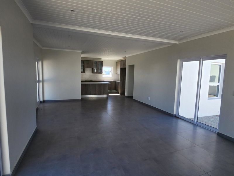 Spacious open-plan living area featuring large format floor tiles, tongue and groove ceiling, and direct access to outdoor areas through sliding glass doors.