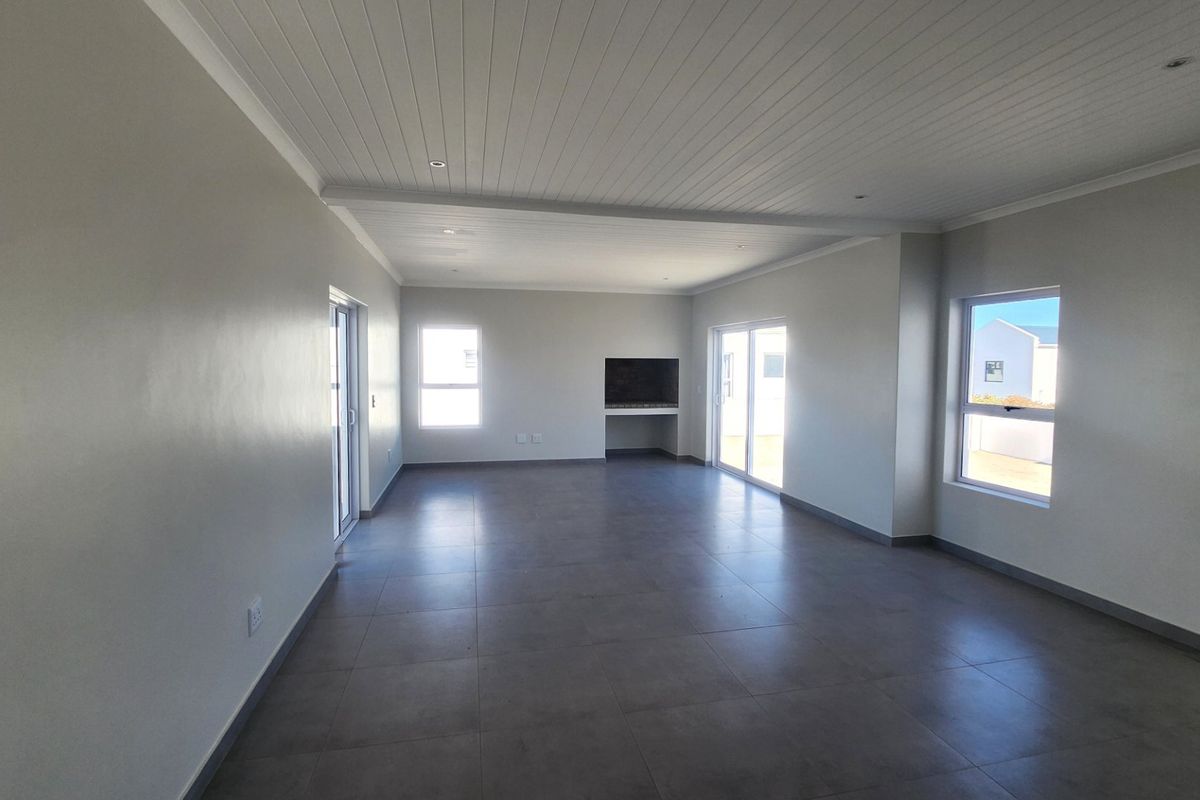 Spacious open-plan living area featuring large format floor tiles, a built-in fireplace, recessed ceiling lighting, and sliding doors providing ample natural light.