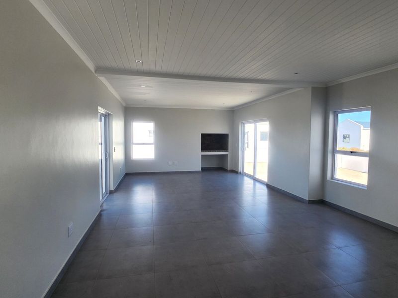 Spacious open-plan living area featuring large format floor tiles, a built-in fireplace, recessed ceiling lighting, and sliding doors providing ample natural light.
