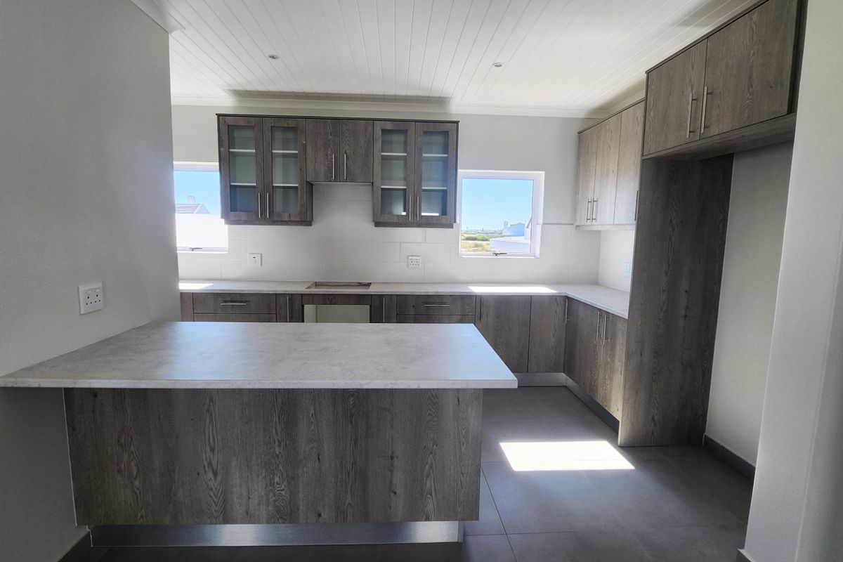 Modern kitchen featuring wood-look cabinetry, stone-effect countertops, a functional breakfast bar, and tiled flooring in a bright, open-plan layout.