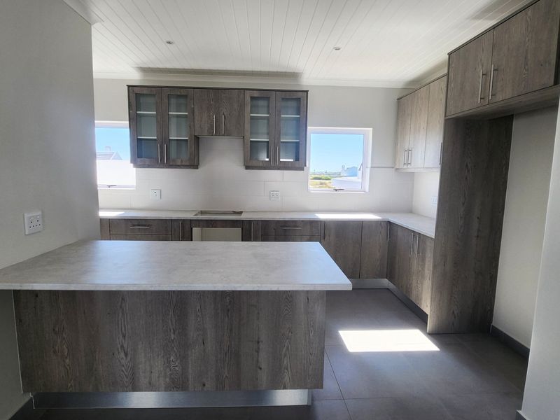 Modern kitchen featuring wood-look cabinetry, stone-effect countertops, a functional breakfast bar, and tiled flooring in a bright, open-plan layout.