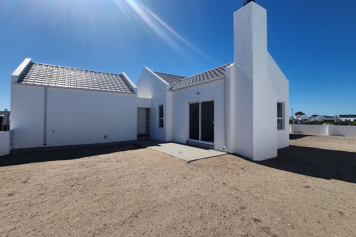 Rear view of a modern white house featuring a tiled roof, prominent chimney, and a paved patio area leading to a sliding glass door.