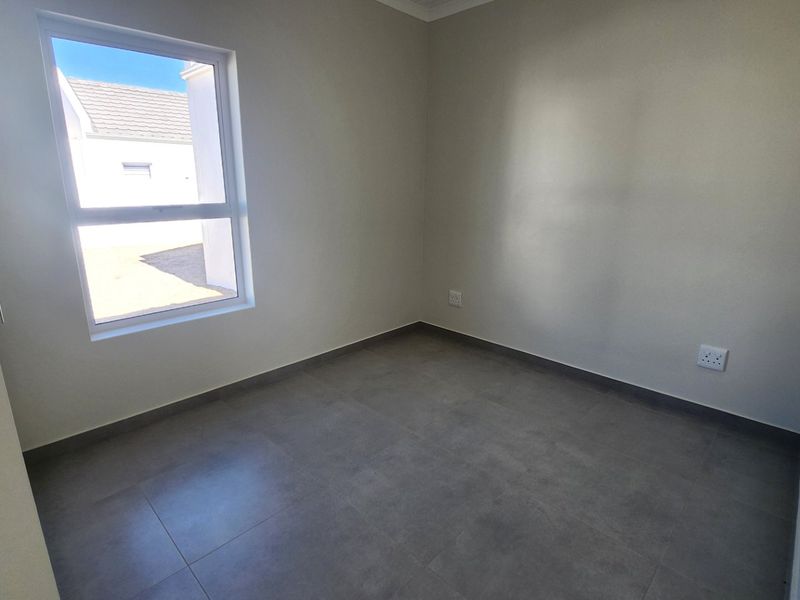 A clean, empty bedroom featuring neutral walls, modern grey floor tiles, and a window providing natural light.