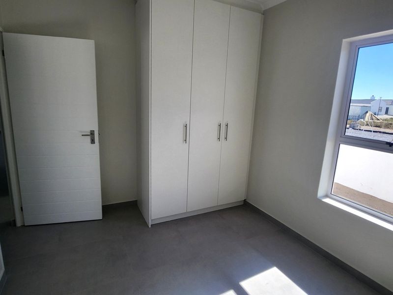 A clean, modern bedroom featuring neutral tiled flooring, a built-in wardrobe, and a large window providing natural light.