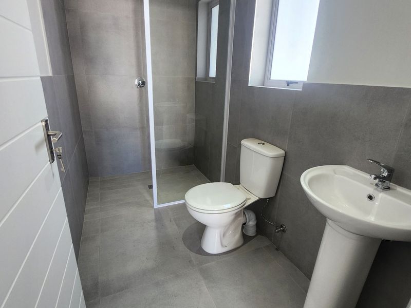 Modern bathroom featuring grey floor-to-ceiling tiling, a walk-in shower with glass screen, a pedestal basin, and a standard toilet.