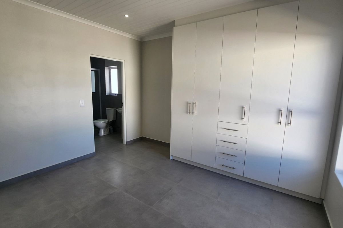 A bright, modern bedroom featuring neutral tiled floors, extensive built-in cabinetry, and direct access to an en-suite bathroom.