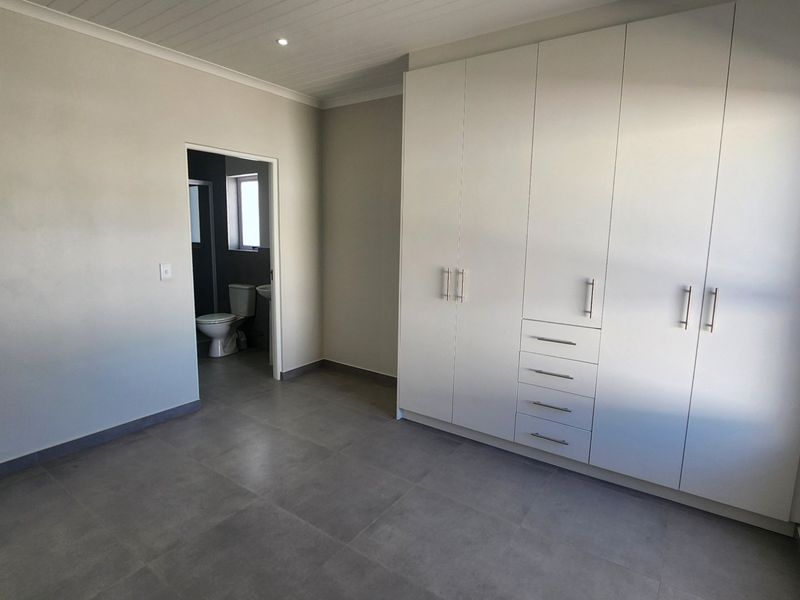 A bright, modern bedroom featuring neutral tiled floors, extensive built-in cabinetry, and direct access to an en-suite bathroom.