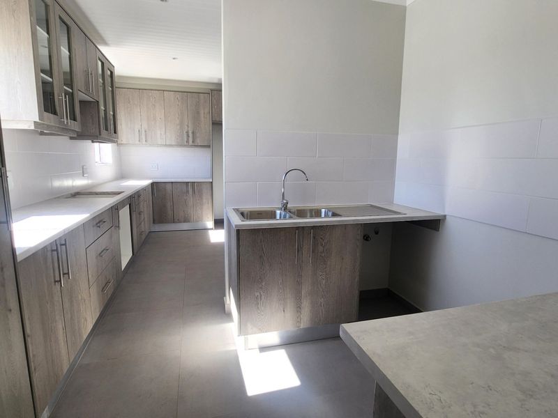 Modern kitchen featuring wood-grain laminate cabinetry, stone-look countertops, a double bowl sink, and clean tiled splashbacks in a bright, open layout.