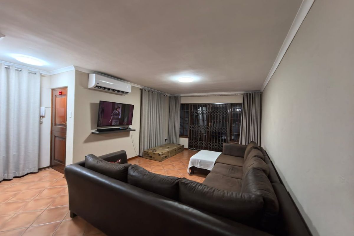 A spacious living room featuring tiled flooring, a wall-mounted air conditioning unit, and a secure entrance with a metal security gate.