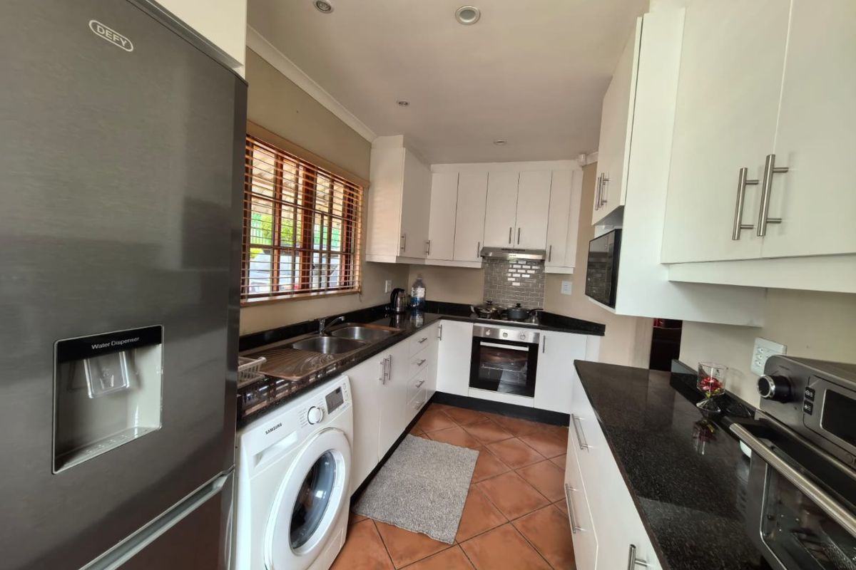 A functional kitchen featuring white cabinetry, dark granite countertops, a built-in oven with hob, and integrated laundry plumbing.