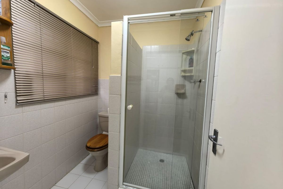 A functional bathroom featuring a glass-enclosed shower, toilet, and basin with tiled finishes and venetian blinds.