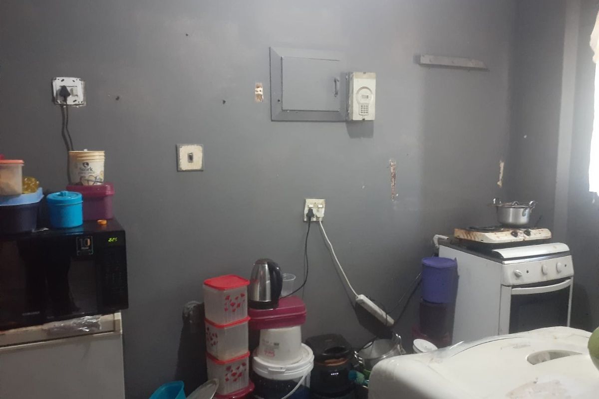 A small kitchen area featuring a freestanding stove and wall-mounted electrical infrastructure, currently showing signs of wear and requiring cosmetic updates.