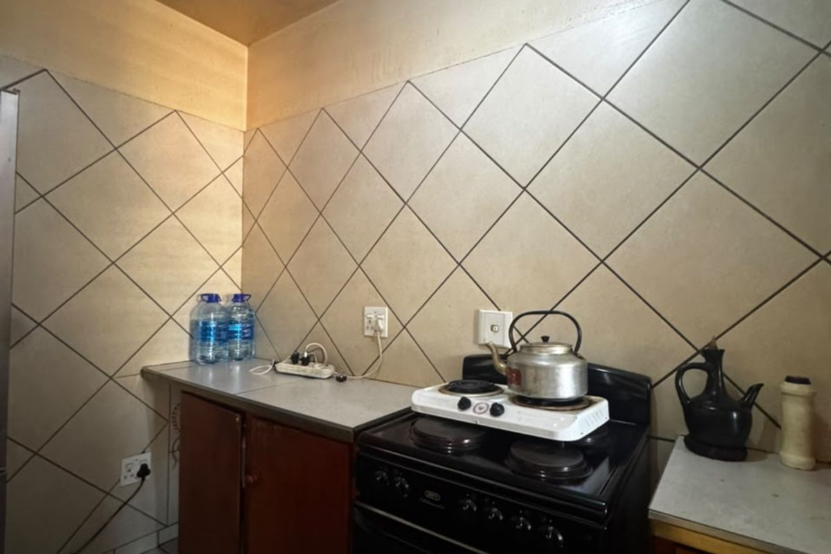 A compact kitchen featuring tiled backsplash, laminate countertops, and built-in cabinetry, requiring cosmetic updates to modernize the space.